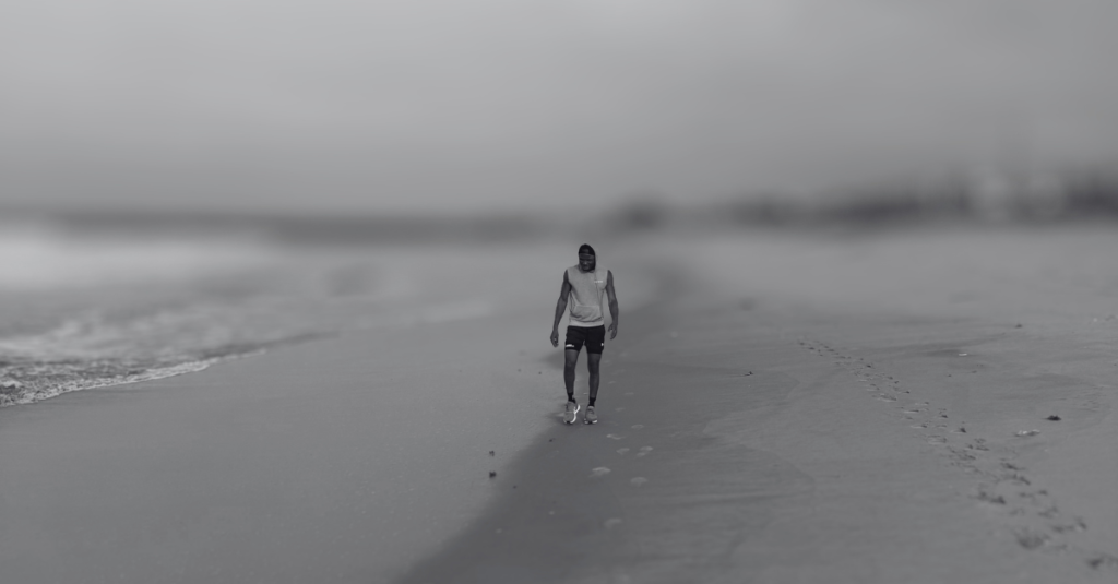 Anthony walking along the beach in the opposite direction, moving steadily during a calm recovery walk, reflecting on Recovery Mistakes After 30.