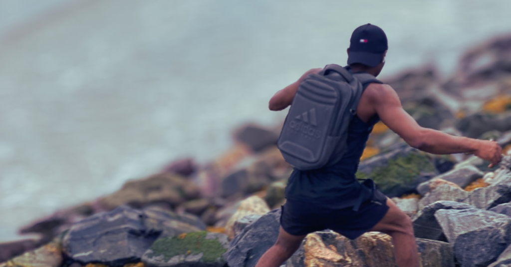 Anthony running along rocks at the beach side, back view, illustrating why most people quit fitness after 30 due to lack of consistency, motivation, and lifestyle challenges.