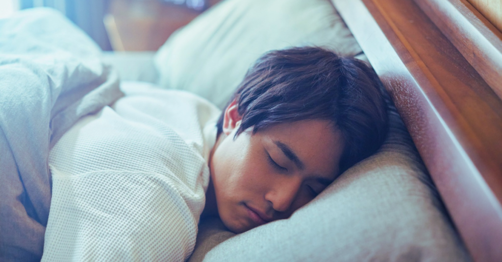 Asian man sleeping peacefully in bed at night, highlighting the importance of healthy sleep habits and avoiding common sleep mistakes after 30.