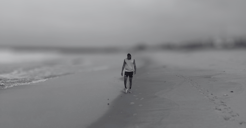 Anthony walking along the beach in the opposite direction, moving steadily during a calm recovery walk, reflecting on Recovery Mistakes After 30.