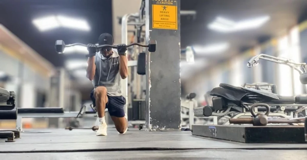 Fitness After 30: Anthony performing a lunge while doing a bicep curl with an EZ bar in the gym.