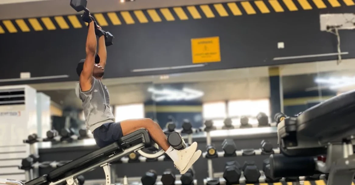 Fitness After 30: Anthony performing an EZ bar shoulder press while using a sit-up machine in the gym.