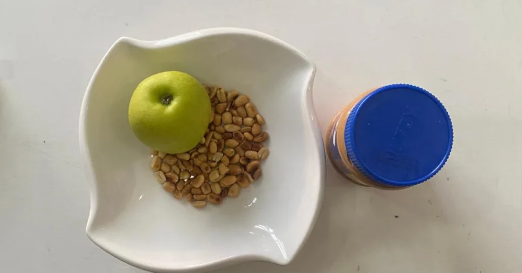 Nutrition After 30: A bowl of groundnuts with an apple and peanut butter beside it, showcasing a healthy snack option for balanced nutrition.