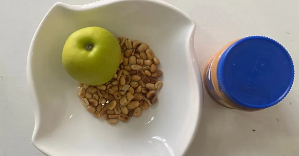 Bowl of high-protein overnight oats topped with apple slices and groundnuts, with a side of natural nut butter.