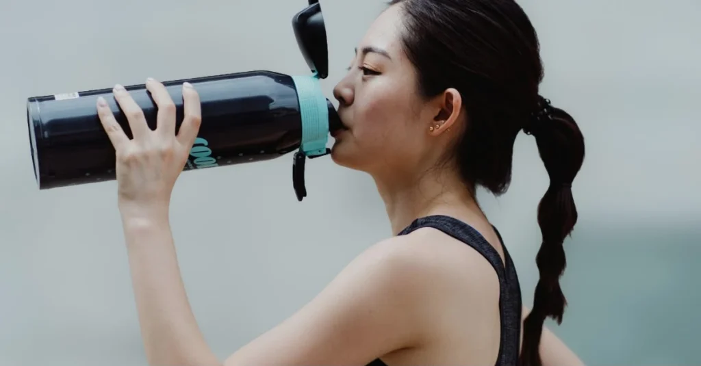 A woman drinking water from a bottle to stay hydrated during exercise.